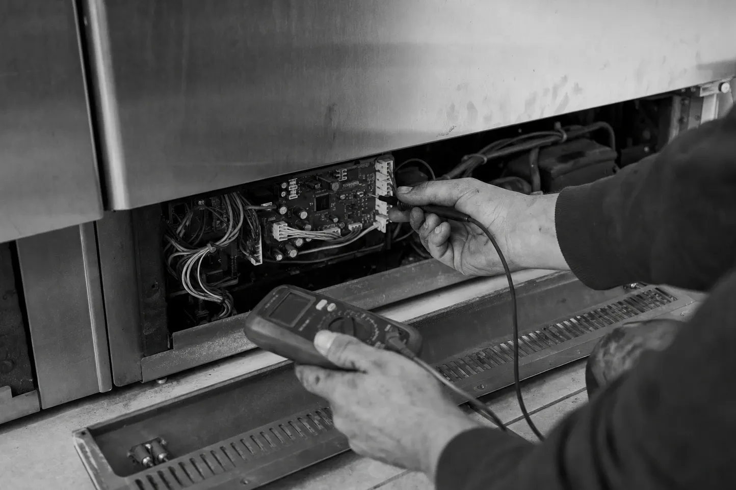 Multimeter probes on the control board behind the lower grille of a built-in, in black and white