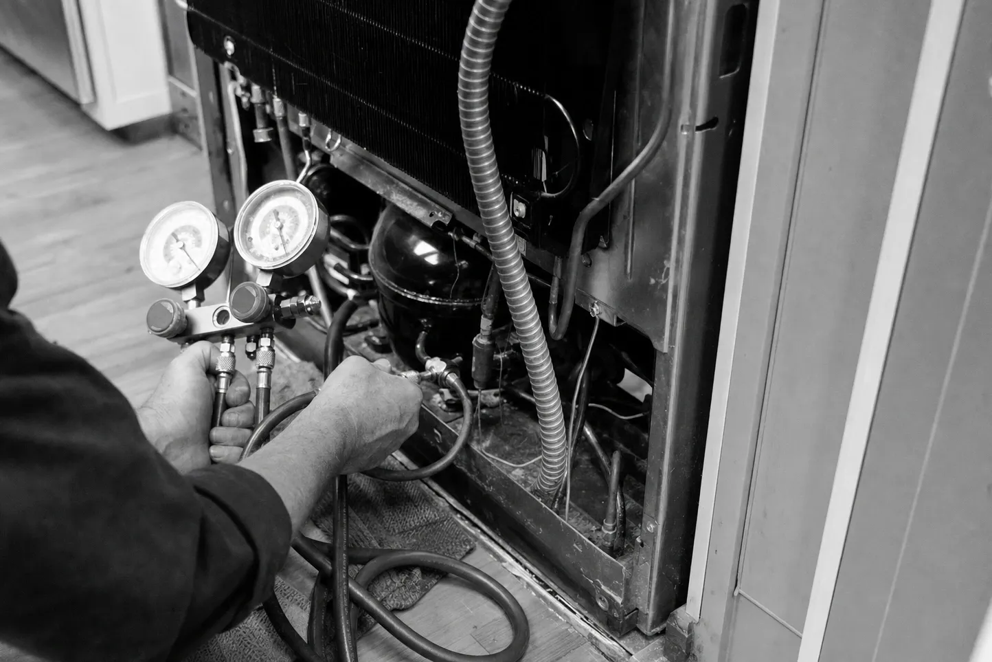 Manifold gauges connected at the compressor of a built-in pulled out from cabinetry, in black and white